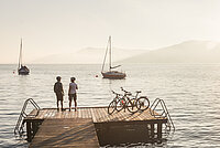 A couple takes a break from cycling and watches the sunset over Lake Attersee