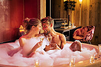 A couple in the hot tub with a glass of sparkling wine in the cosy suite at the Hotel Winzer